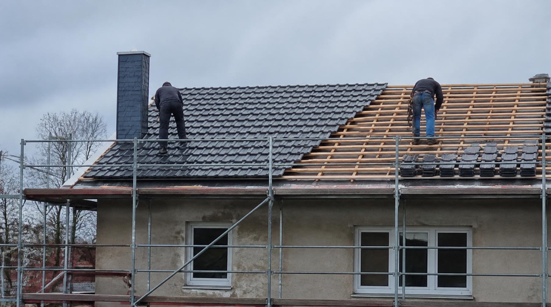 Zwei Handwerker decken die Dachfläche eines eingerüsteten Wohnhauses bei bedecktem Wetter